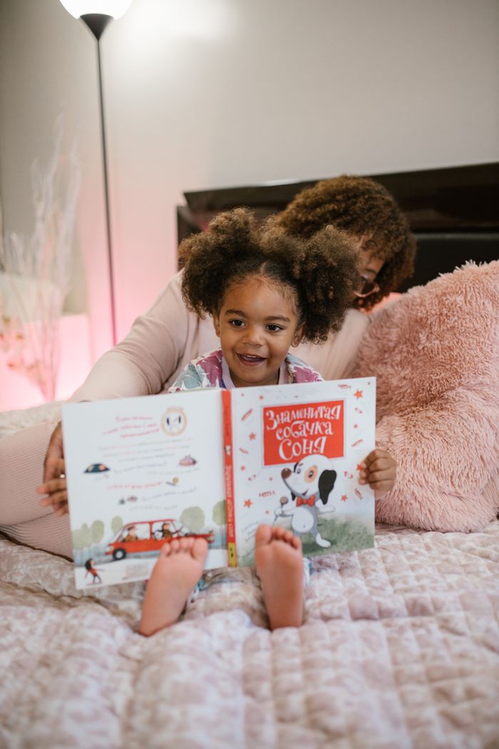 A mother and daughter enjoy reading a bedtime story, creating a cozy and intimate moment on the bed.